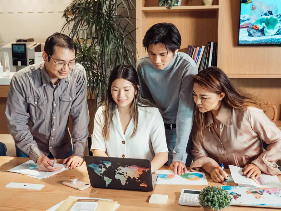Equipe reunida em torno de um notebook com o mapa-múndi, planejando operações internacionais